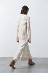 Vestido midi de punto en color gris, con diseño de tejido acanalado vertical, cuello redondo y mangas largas. Presenta una silueta recta y fluida.