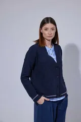 Saco tejido en lambswool con diseño de rombos y trenzas en el frente. Presenta cierre frontal con botones, cuello en V y detalles de rayas en contratono en puños y ruedo. Incluye pin bordado en la manga.