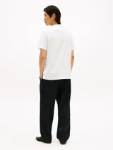 Remera de algodón blanco con cuello redondo y manga corta. Presenta una banda horizontal negra en el pecho con el nombre de la marca estampado en tipografía cursiva blanca.