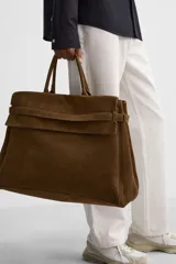 Bolso de mano extragrande color marrón oscuro, estilo tote o satchel, fabricado en piel. Presenta dos asas de mano y un detalle de cinta ajustable con cierre de solapa en la parte frontal superior.