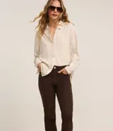 Pantalón slim de jean marrón, de cintura mediana con cierre frontal de cremallera y botón, bolsillos y trabillas para cinturón.