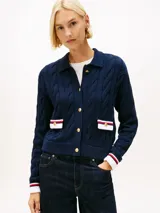 Cárdigan de punto trenzado en color azul marino, con cuello tipo polo y cierre frontal de botones dorados. Presenta dos bolsillos frontales con solapas decoradas en blanco, rojo y azul, y puños con el mismo detalle tricolor.