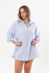 Vestido camisero de lino color celeste, con escote en V, cuello clásico, cierre frontal de botones y mangas tres cuartos regulables. Diseño holgado con corte asimétrico.