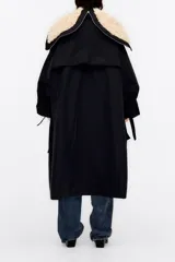 Gabardina larga acolchada color negro con cuello de piel sintética color crema, chaleco interior desmontable con cierre de cremallera, cierre frontal con botones, mangas largas con lazos en los puños y logo bordado en el pecho.