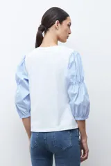 Remera de algodón con cuerpo liso en color blanco y mangas abullonadas de tela camisera con estampado de rayas finas en azul y blanco.