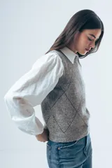 Chaleco de punto gris con diseño de rombos bordados en negro y cuello redondo. Presenta un corte clásico y tejido de textura suave.