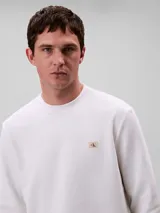 Buzo de Calvin Klein color blanco, confeccionado en algodón regenerado, con cuello redondo, puños y dobladillo de punto canalé y un mini monograma en parche en el pecho.