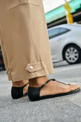 Pantalón de tiro alto estilo paperbag en color beige, con pinzas frontales y cinturón de la misma tela. Presenta bolsillos laterales tipo cargo con solapa y pernera ajustable con botones en el bajo.