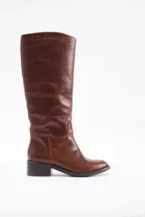 Bota de caña alta confeccionada en cuero vacuno color marrón, con taco cuadrado bajo y punta redondeada.