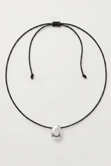 Collar con cordón negro ajustable y dije colgante ovalado de metal plateado con diseño irregular.