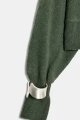 Sweater de punto color verde militar, con cuello asimétrico y manga larga con brazalete metálico en el puño.