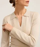 Blusa de punto ajustada color negro, con cuello polo y escote pronunciado en V. Presenta un tejido acanalado vertical en el torso y mangas largas.