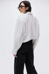 Pantalón de pana de algodón color negro, de tiro alto, con pliegues delanteros y traseros. Cierre con dos botones dorados, bolsillos traseros abiertos y piernas rectas.