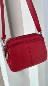 Bandolera de símil cuero color rojo, con doble bolsillo principal, un bolsillo frontal y un bolsillo trasero. Incluye correa ajustable.
