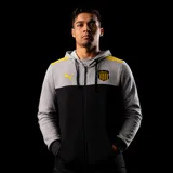 Buzo con cierre frontal y capucha, diseño de bloques de color gris en la parte superior y negro en la inferior, con detalles en amarillo en los hombros. Incluye el logo de Puma y el escudo del Club Atlético Peñarol.