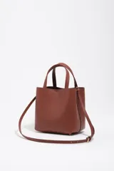 Bolso bandolera de tamaño pequeño de cuero marrón, con asas de mano, asa ajustable y logo grabado en dorado en el frente.