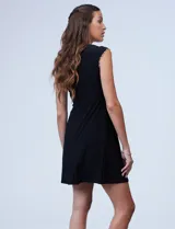 Vestido corto negro de seda fría, con escote a la base y mangas cortas. Apliques de perlas en escote y mangas.