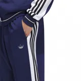 Pantalón deportivo azul con tres rayas blancas verticales a los costados y logo de Adidas bordado en blanco.