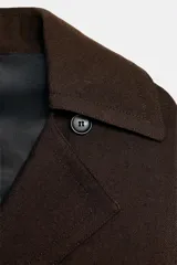 Trench fluido de corte recto confeccionado en lana, con cuello solapa, manga larga, bolsillos delanteros y cinturón ajustable del mismo tejido.