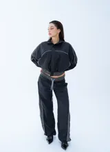 Campera rompeviento negra de estilo deportivo, con cierre frontal completo, cuello alto y detalles de líneas blancas en los hombros y mangas. Presenta puños y cintura elásticos en tono gris oscuro.