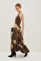 Vestido largo de corte fluido con estampado estilo batik en tonos oscuros, marrones y crema. Presenta un diseño inspirado en pañuelos con volado en el ruedo y escote en V.