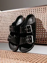 Sandalia plana Genuins modelo Honolulu, de color negro con tachas metálicas decorativas. Cuenta con dos tiras ajustables con hebillas plateadas, plantilla anatómica de corcho natural y suela de EVA.
