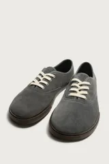 Zapatilla deportiva barefoot fabricada en piel con acabado serraje de color marrón, con cordones en contraste y suela fina de goma.