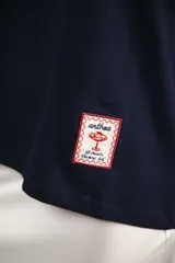 Remera de algodón color azul marino, corte relajado con hombro caído. Presenta cuello redondo blanco y bordado a mano en contraste en los puños de las mangas. Tiene un parche bordado en la parte inferior del frente.