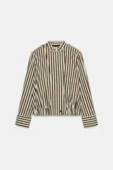 Camisa tipo bomber confeccionada en algodón, con diseño de rayas verticales en tonos marrón y blanco. Presenta cuello perkins, manga larga con puños, bolsillo de plastrón con solapa en el frente, bajo elástico y cierre frontal con botones.