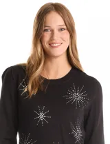 Buzo de punto liviano color blanco, con cuello redondo y mangas largas con frunce en los hombros. Presenta apliques de strass en forma de estrellas o destellos en el frente y puños y cintura acanalados.