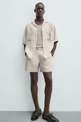 Bermuda de corte relajado color beige claro, confeccionada en lino. Presenta cintura elástica con cordón ajustable y bolsillos laterales y traseros.