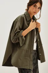 Camisa verde militar de algodón, con cuello camisero, botones frontales, mangas largas con puños abotonados y bolsillos de parche en el pecho. Presenta aberturas laterales en el dobladillo.