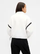 Buzo de polar tipo sherpa color marrón, con cuello alto y cierre frontal parcial. Presenta el logo de la marca bordado en el pecho y detalles de costuras reforzadas en hombros y mangas.