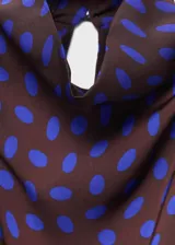 Blusa sin mangas de corte recto con cuello drapeado y cierre de botones. Presenta un diseño estampado de lunares en color azul sobre fondo oscuro.
