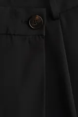 Pantalón sastrero negro de corte holgado, con diseño cruzado asimétrico en el frente, pinzas y piernas amplias.