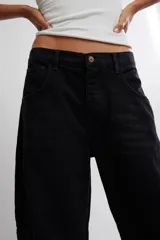 Jean de silueta barrel y tiro medio, confeccionado en denim negro rígido de caída estructurada. Presenta diseño de cinco bolsillos, cierre frontal con botón y costuras estratégicas que definen el volumen amplio de la pierna que se afina hacia los tobillos.