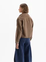 Chaqueta de gabardina color marrón, con cuello camisero, cierre frontal con botones metálicos, bolsillos frontales y mangas abullonadas con puños rectos.