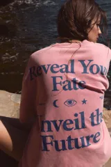 Camiseta oversize de manga corta y cuello redondo, color rosado con efecto lavado, con pequeño texto estampado en azul en el pecho.