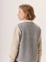 Buzo de lana con diseño bicolor, presentando un panel frontal en color beige y un panel posterior en color gris. La prenda destaca por su textura tejida con patrón de rombos y cuello redondo.