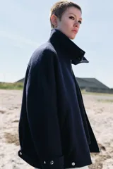 Chaqueta bomber de corte holgado confeccionada en tejido con lana, color azul marino. Presenta cuello subido, cierre frontal con cremallera metálica, bolsillos delanteros y detalle de trabillas con botones metálicos en el ruedo.
