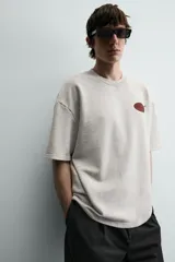 Sudadera gris de corte relaxed fit, cuello redondo y manga corta. Presenta un estampado en el pecho con la frase "Tokyo Kitchen" en un óvalo rojo con palillos.