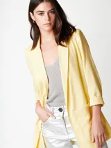 Blazer amarillo pálido de corte recto y holgado, con hombreras finas, bolsillos delanteros y lazo de algodón a tono para cerrar.