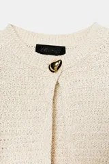 Chaqueta de punto de hilo metalizado color beige con cuello redondo, manga larga y cierre frontal con un botón dorado.