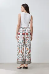 Pantalón de corte recto con estampado floral en tonos naranja, rojo, verde y marrón sobre fondo blanco. Presenta cintura elástica y ruedo con diseño geométrico.