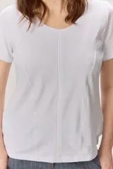Remera de manga corta con diseño colorblock en tonos blanco, negro y beige, escote redondo y costuras verticales decorativas en el centro.