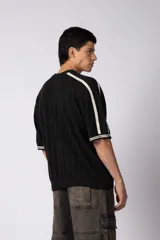 Remera de tejido de punto con textura calada, color crema con rayas verticales sutiles. Presenta cuello en V, mangas cortas con franjas laterales en color marrón oscuro y logo bordado en el centro del pecho.