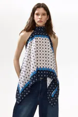 Top halter confeccionado en viscosa satinada de corte evasé, con cuello elevado, cintas para enlazar en la nuca, bajo redondeado y estampado geométrico en tonos azul marino, celeste y blanco.