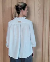Blusa de manga larga con estampado de rayas verticales finas en tono beige. Presenta cuello redondo con volados, cierre frontal parcial con botones y puños con volados.
