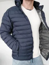 Campera puffer azul marino con capucha, cierre frontal con cremallera, bolsillos laterales con cremallera y forro térmico plateado. Diseño acolchado horizontal.