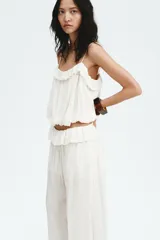 Pantalón oversized de tiro bajo color blanco crudo, confeccionado en viscosa con alforzas, ribetes de encaje, cordón de ajuste y ribete de volado en la cintura.